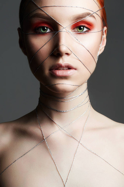 Fashion portrait of beauty make-up girl with orange eye shadow. Beautiful young Woman with makeup and silver thread on the face and Body - Foto, Imagem