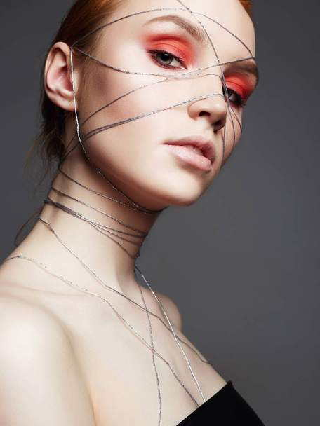 Fashion portrait of beauty make-up girl with orange eye shadow. Beautiful young Woman with makeup and silver thread on the face and Body - Foto, afbeelding