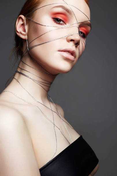 Fashion portrait of beauty make-up girl with orange eye shadow. Beautiful young Woman with makeup and silver thread on the face and Body - Photo, Image
