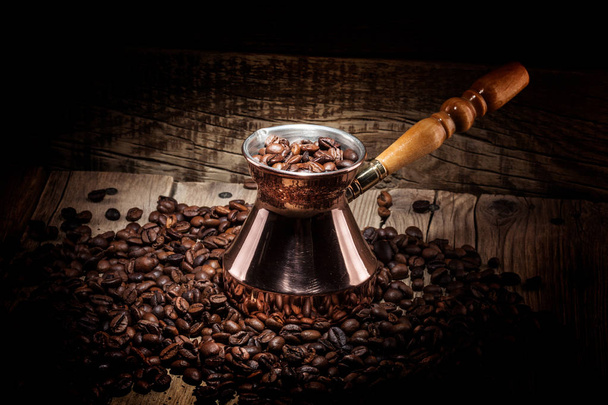 scattered coffee beans and copper coffee turk on wooden background - Photo, Image