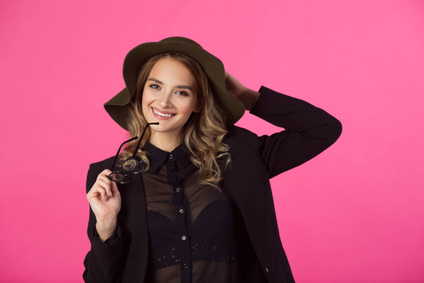 beautiful young joyful girl in a black jacket and hat on a pink background - Photo, Image
