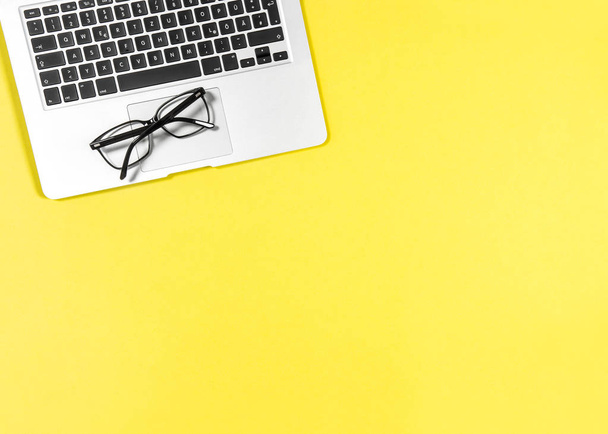 Office workplace. Minimal flat lay mockup. Laptop and glasses on yellow background - Fotó, kép