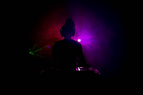 DJ dreht, mischt und kratzt in einem Nachtclub, Hände von DJ zwicken verschiedene Track-Controller auf dem Deck, Blitzlicht und Nebel, oder DJ mischt den Track im Nachtclub bei Party. Selektiver Fokus - Foto, Bild
