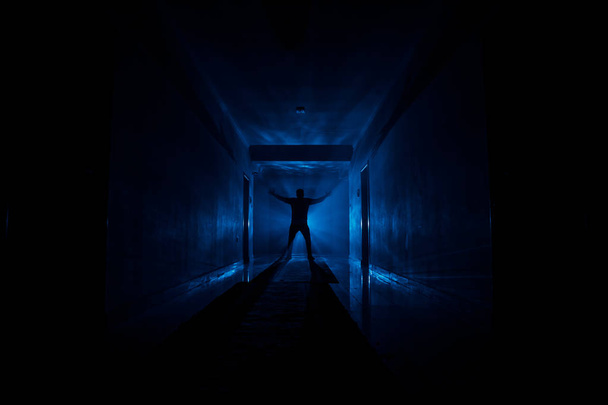 Ανατριχιαστικό σιλουέτα στο σκοτεινό εγκαταλελειμμένο κτίριο. Τρόμου σχετικά με μανιακός έννοια ή σκοτεινός διάδρομος με πόρτες γραφείων και φώτα με σιλουέτα του τρόμου τρομακτικό πρόσωπο που στέκεται με διαφορετικές πόζες. - Φωτογραφία, εικόνα