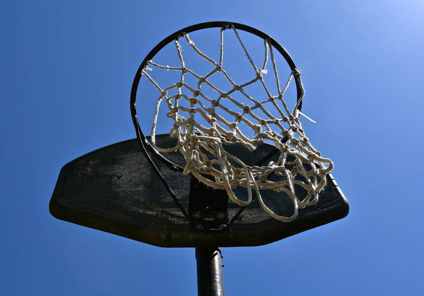 A torn net hangs from a basketball rim and backboard.  - Фото, зображення