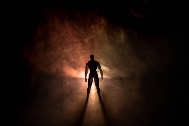 Silhueta de homem em pé sobre um fundo enevoado escuro tonificado. Foto decorada com figura de homem na mesa com luz. Foco seletivo
 - Foto, Imagem