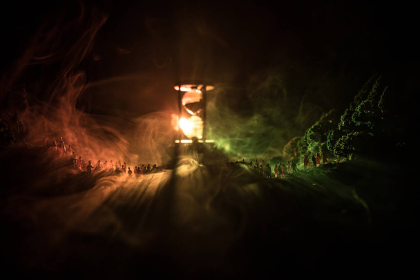大勢の霧の背景にトーンの光ビームと大きな砂時計に対して在泊でフォレストの人のシルエット。時間の概念。砂時計の通過時間を測定 - 写真・画像