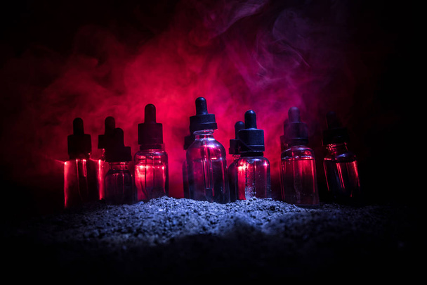 Vape concept. Smoke clouds and vape liquid bottles on dark background. Light effects. Useful as background or vape advertisement or vape background. Selective focus - Photo, Image