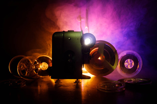 Old style movie projector, still-life, close-up. Film projector on a wooden background with dramatic lighting and selective focus. Movies and entertainment concept - Фото, изображение