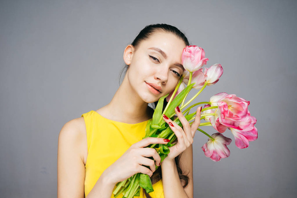 beautiful elegant girl in a yellow dress is holding a bouquet of fragrant flowers, posing and looking at the camera - Photo, image