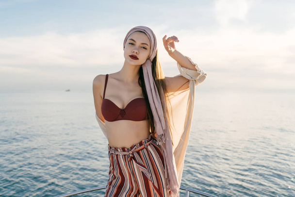 an attractive elegant girl with a headscarf on her head swims on her white yacht on the Caribbean sea, posing - Foto, imagen