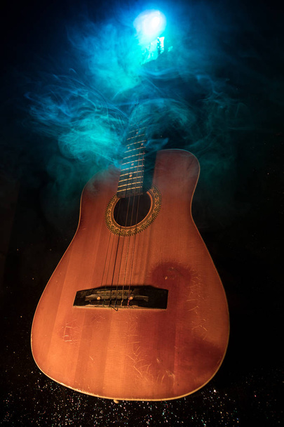 Concepto musical. Guitarra acústica sobre fondo oscuro bajo haz de luz con humo. Guitarra con cuerdas, de cerca. Enfoque selectivo. Efectos de fuego
. - Foto, Imagen