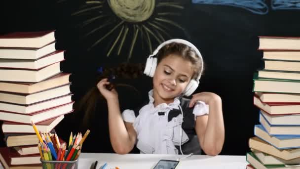 現代の学校のコンセプトです。魅力的な女の子は、うずたかく積まれた本と机に座っています。彼女の背後にある黒板。クラスの女子高生 - 映像、動画
