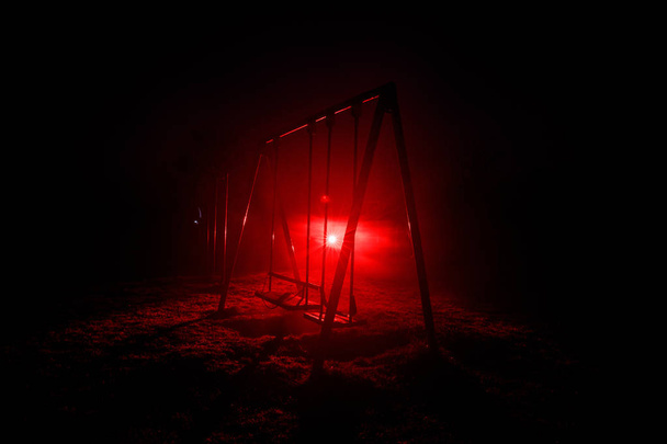 Nachtfoto einer Metallschaukel, die nachts im Freien steht, mit Nebel und surreal getöntem Licht auf dem Hintergrund. Niemand da. Konzept der Einsamkeit - Foto, Bild