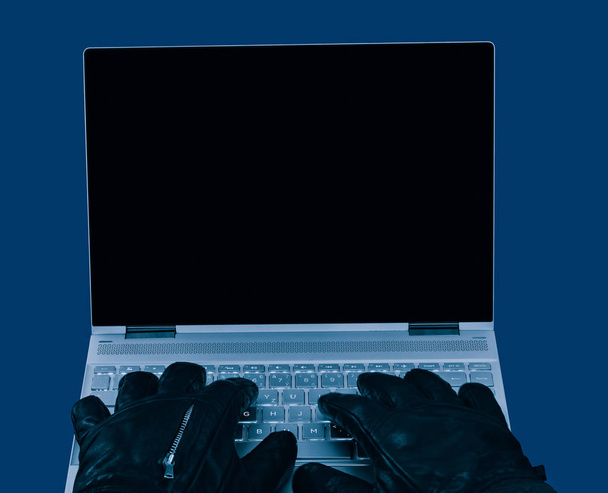 Laptop a ruce v černé kožené rukavice detail. Kopírování místo na tmavý displej. Koncept hackování, špionáž, cenzura, sabotáž, ochrana údajů, bezpečnost, Gdpr. izolovaná na modrém pozadí. - Fotografie, Obrázek