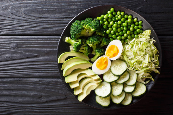 Delicious green salad of fresh avocado, peas, cabbage, cucumber, eggs and broccoli close-up on a plate. Horizontal top view from abov - Photo, Image