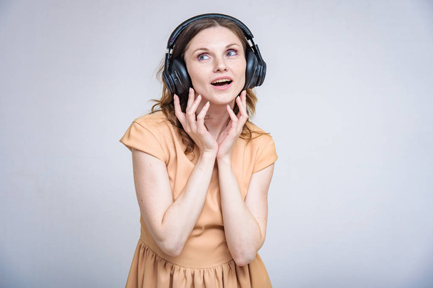 I like listening to music on headphones. Portrait of beautiful brunette girl on white background listening music with headphones. She is standing right in front of the camera smiling and looking happy - Photo, Image