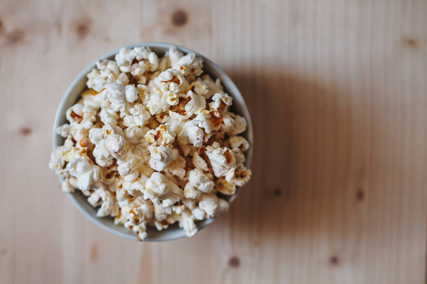 A bowl filled with popcorn placed on a light wooden table surface. Shallow depth of field. Top view. - Foto, afbeelding