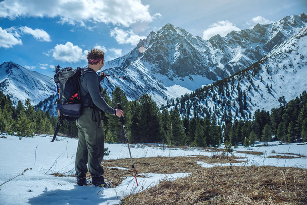 Man Hiker with trekking poles stands in the snowy mountains at the foot of the peak in Sunny weather. The concept of travel and achieve the goal - Photo, Image