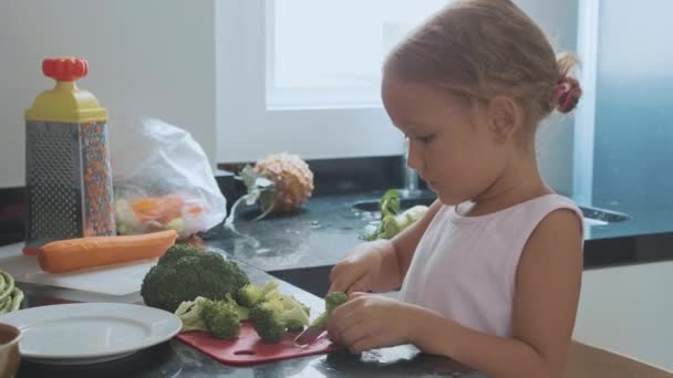 Little child girl cutting brocoli for cooking at domestic kitchen. - Video