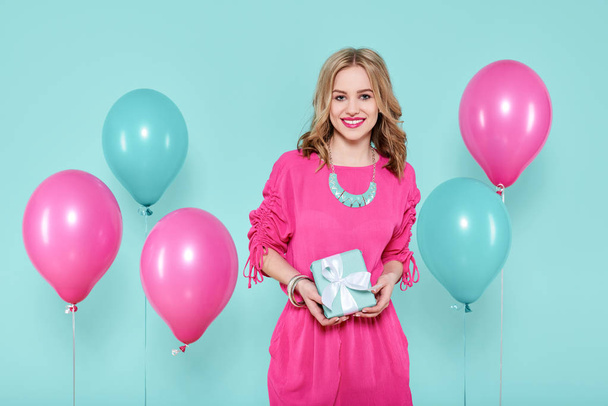 Gorgeous young woman in party outfit holding a present isolated over pastel blue colored background. Birthday Party concept. - Zdjęcie, obraz