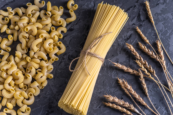 Kypsentämätön italialainen pasta spagetti ja cavatappi spikelets durumvehnää tummalla taustalla. Elintarvikemuotoilun koostumuksen käsite
. - Valokuva, kuva