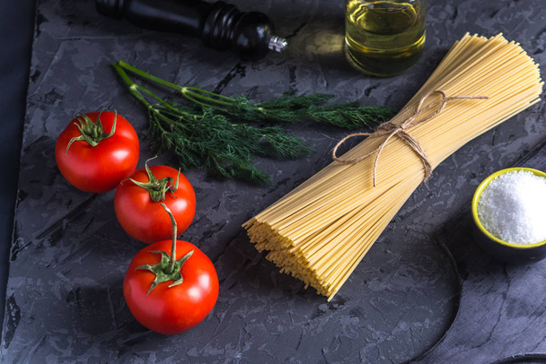 Uncooked italian pasta spaghetti with ingredients for tomato sauce on a dark background. The concept of the composition of food design. - 写真・画像