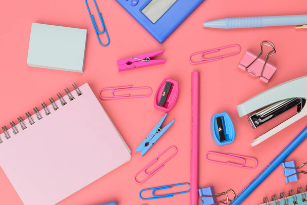 Stationary concept, Flat Lay top view Photo of Scissors, pencils, paper clips,calculator,sticky note,stapler and notepad in pink and blue tone on pink background with copy space. - Foto, imagen