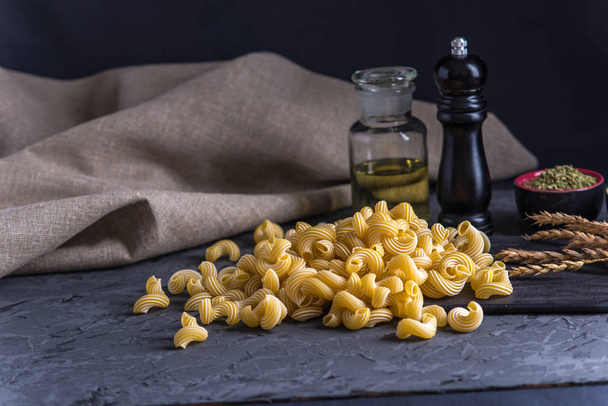 Uncooked Italian pasta spaghetti and ingredients for cooking in the kitchen on a dark background. The concept of the composition of food design. - Photo, Image