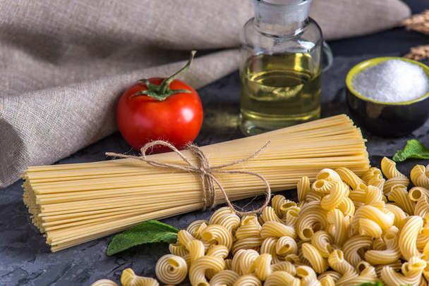 Uncooked italian pasta cavatappi and spaghetti with ingredients for tomato sauce on a dark background. The concept of the composition of food design. - Photo, Image