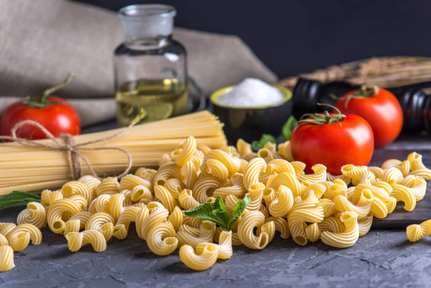 Uncooked italian pasta cavatappi and spaghetti with ingredients for tomato sauce on a dark background. The concept of the composition of food design. - Photo, Image