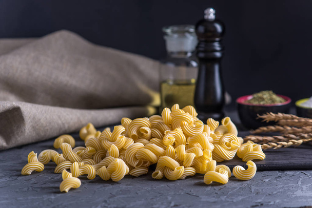 Kypsentämätön italialainen pasta spagetti ja ainesosat ruoanlaittoon keittiössä tummalla pohjalla. Elintarvikemuotoilun koostumuksen käsite
. - Valokuva, kuva