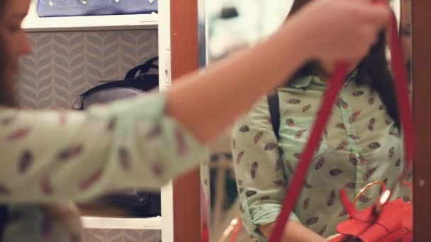 A young woman in a store is choosing a bag, standing by the mirror in the store - Filmagem, Vídeo