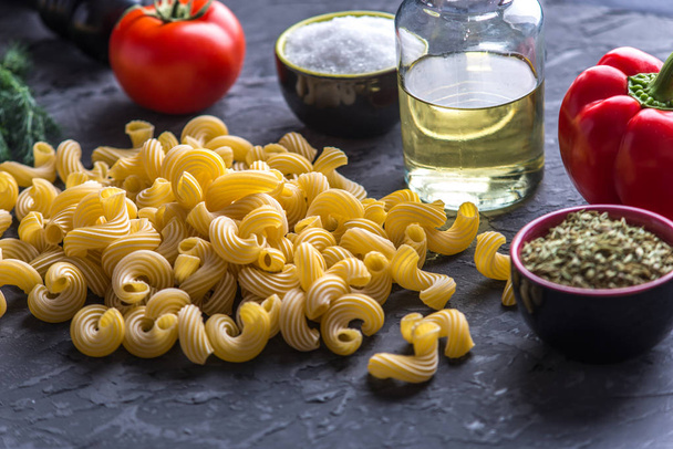 Kypsentämätön italialainen pasta cavatappi, jossa on tomaattikastikkeen ainesosia tummalla pohjalla. Elintarvikemuotoilun koostumuksen käsite
. - Valokuva, kuva