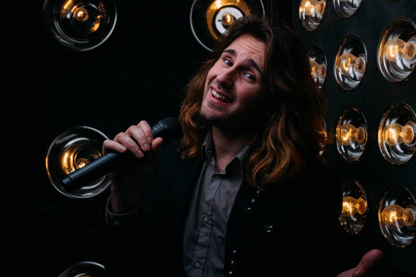 Brutal singer with microphone on the stage, with long hair, against the background of bright lanterns, scene - Foto, imagen