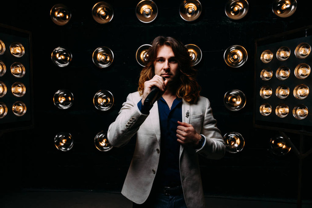 men singer with microphone on the stage, with long hair, against the background of bright lanterns, scene - Fotografie, Obrázek