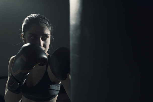 Young woman doing boxing training at the gym, she is wearing boxing gloves and hitting the punching bag - Фото, зображення
