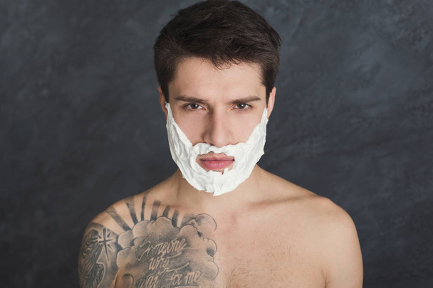 Serious tattooed man with foam on face - Фото, изображение