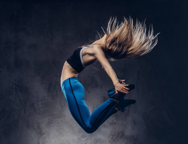 Молода балерина в спортивному одязі танцює і стрибає в студії. Ізольовані на темному тлі
. - Фото, зображення