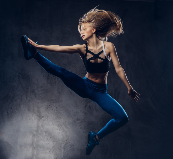 Young ballerina in sportswear dances and jumps in a studio. Isolated on a dark background. - Foto, Imagen