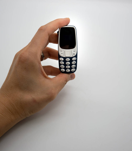 Nő kezében a világ legkisebb mobil telefon-val Oled képernyő kék műanyag test elszigetelt fehér background - Fotó, kép
