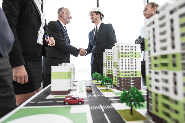 Business people standing near residential quarter houses models and shaking hands, meeting of architects and investors - 写真・画像
