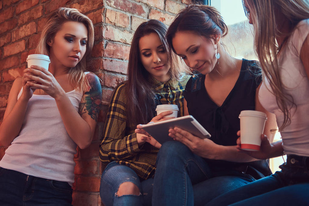 Grupo de amigas em roupas casuais discutindo enquanto procuravam algo em um tablet digital em um quarto com um interior loft
. - Foto, Imagem