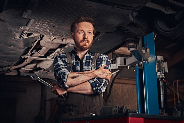 Automonteur gekruist handen terwijl je onder de opheffing van de auto in een garage voor reparatie. - Foto, afbeelding