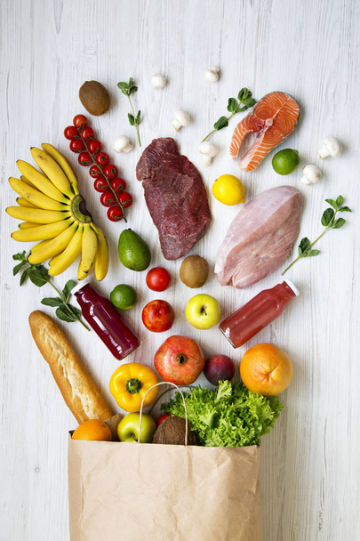 Bolsa de papel de diferentes frutas y verduras en la superficie de madera blanca. Fondo de comida saludable, vista superior. Alimentación saludable
. - Foto, imagen