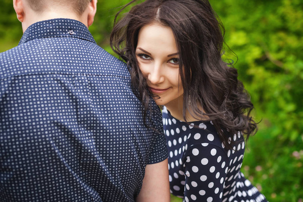 Happy young couple hugging in nature. girl with long brunette hair wearing black dress in white peas, man in blue shirt in pattern - Photo, image