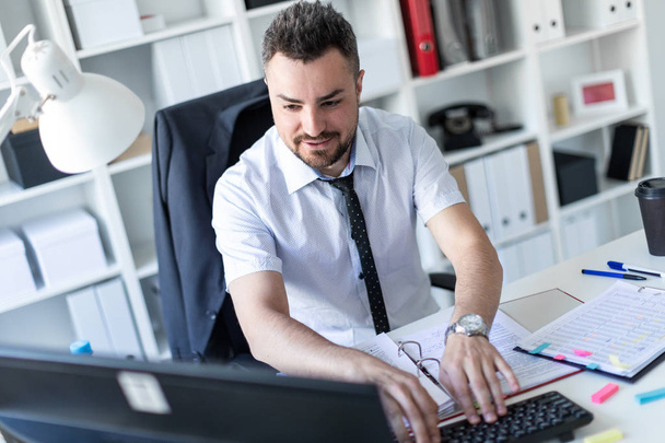 Een man zit aan een tafel in het kantoor, werken met documenten en een computer. - Foto, afbeelding