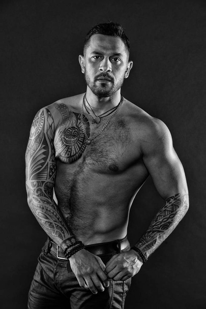 Man with sexy bare torso in jeans. Bearded man with tattooed body. Tattoo model with six pack or ab. Athlete or sportsman with muscular chest and belly. Sport or fitness bodycare, black and white. - Photo, image