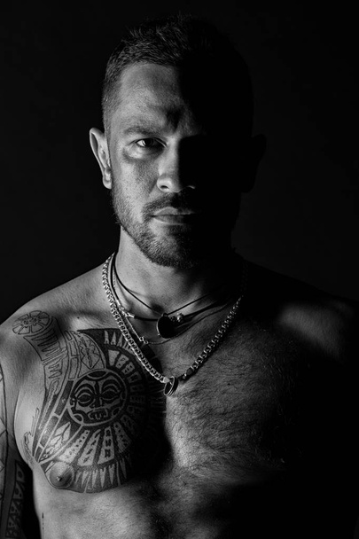 Man with sexy muscular torso. Bearded man with tattooed chest. Fit model with tattoo design on skin. Sportsman or athlete with stylish beard and hair. Bodycare or wellness and sport, black and white. - Fotoğraf, Görsel