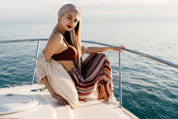 beautiful attractive girl with a headscarf sits on a white yacht, sails on an island on vacation - Foto, afbeelding